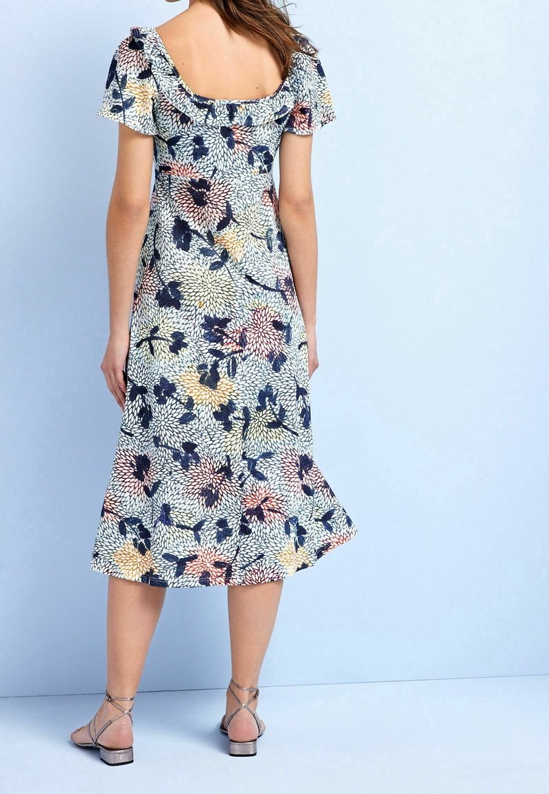 Robe fleurie avec manches courtes, dos carré et ourlet évasé. Couleurs : bleu marine, rose, jaune et crème. Sandales à lanières.