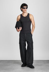 Μαύρο αμάνικο μπλουζάκι, υπερμεγέθη παντελόνια cargo με πλαϊνές τσέπες και μαύρα αθλητικά παπούτσια. Κρατάει μια μικρή μαύρη τσάντα. Κοντά σγουρά μαλλιά και γυαλιά ηλίου.