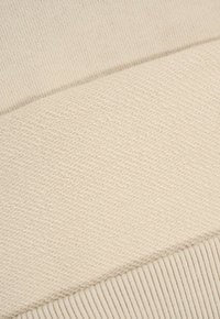 Zbliżenie beżowej dzianiny, pokazujące różnorodne wzory i tekstury splotu z detalami ścięcia.