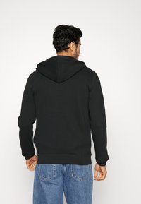 Zwarte hoodie met een relaxte fit. Katoenmengsel, ribgebreide manchetten en onderzoom. Draagt met blauwe spijkerbroek.