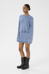 Vestido de suéter azul claro tejido con diseño de punto de cable, cuello redondo y mangas largas. Combinado con botas de cuero negras hasta el tobillo.