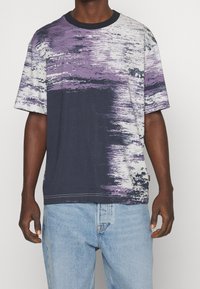 Tričko s krátkým rukávem v námořnické modré a fialové barvě s texturovaným abstraktním vzorem, kulatým výstřihem a viditelnými detaily šití.