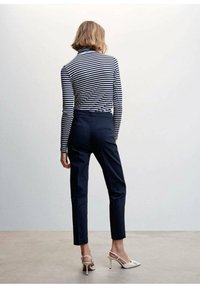 Pull à col roulé rayé bleu marine et blanc, associé à un pantalon bleu marine parfaitement ajusté. Chaussures : sandales à talons gris clair avec un détail en noeud.