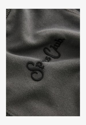 Szary materiał o gładkiej teksturze z czarnym haftowanym napisem "Sea's Club", prezentujący prosty, minimalistyczny design.