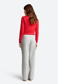 Czerwony sweter wykonany na drutach z długimi rękawami, zestawiony z jasnoszarymi spodniami typu wide-leg z kieszeniami cargo. Uzupełnieniem outfit'u są jasne buty.