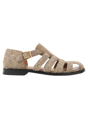 Sandalia plana beige texturizada con suela negra, múltiples tiras cruzando el pie y cierre con hebilla dorada en el lateral.