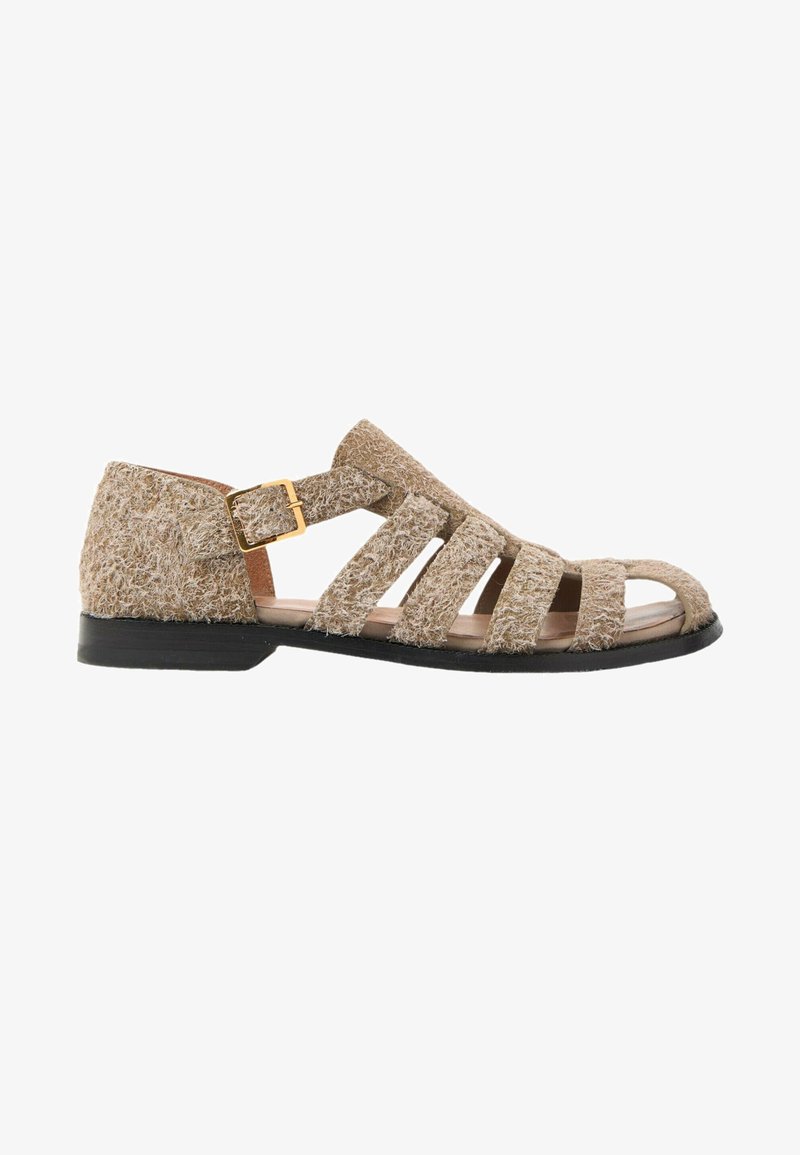 Sandale plate beige texturée avec une semelle noire, plusieurs lanières sur le pied et une fermeture à boucle dorée sur le côté.