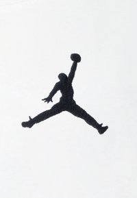 Zwart geborduurd Air Jordan-logo op een witte stoffen achtergrond, met een figuur in de lucht met één uitgestrekte arm die een basketbal vasthoudt.