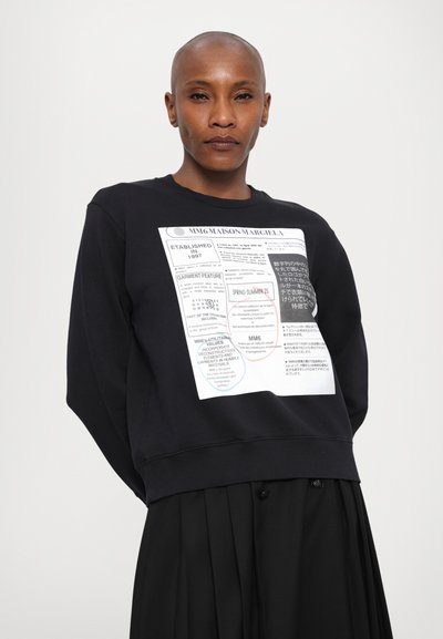 Μαύρη μπλούζα με γραφικό τύπωμα που περιλαμβάνει κείμενα σε πολλές γλώσσες, στρογγυλή λαιμόκοψη και  ribbed μανίκια. Συνδυάζεται με φούστα πλισέ.