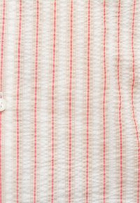 Tissu à rayures verticales rouges, beiges et blanches, présentant un motif texturé subtil et un bouton blanc sur le côté gauche.