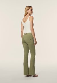 Muotoon ommeltu, ribbitekoinen valkoinen hihaton paita, jossa on pyöreä selkäosa, yhdistettynä korkeavyötäröisiin, oliivinvihreisiin levennettyihin housuihin ja läpinäkyviin korkokengiin.