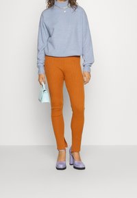 Ljusblå oversized tröja, ribbade orange leggings och lavendelfärgade plattformsskor. En liten ljusblå handväska fulländar looken.