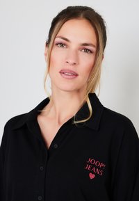 Czarna koszulka polo z kołnierzykiem, z czerwonym nadrukowanym logo "JOOP! JEANS" oraz sercem. Zapięcie na guziki z przodu i miękka tekstura tkaniny.