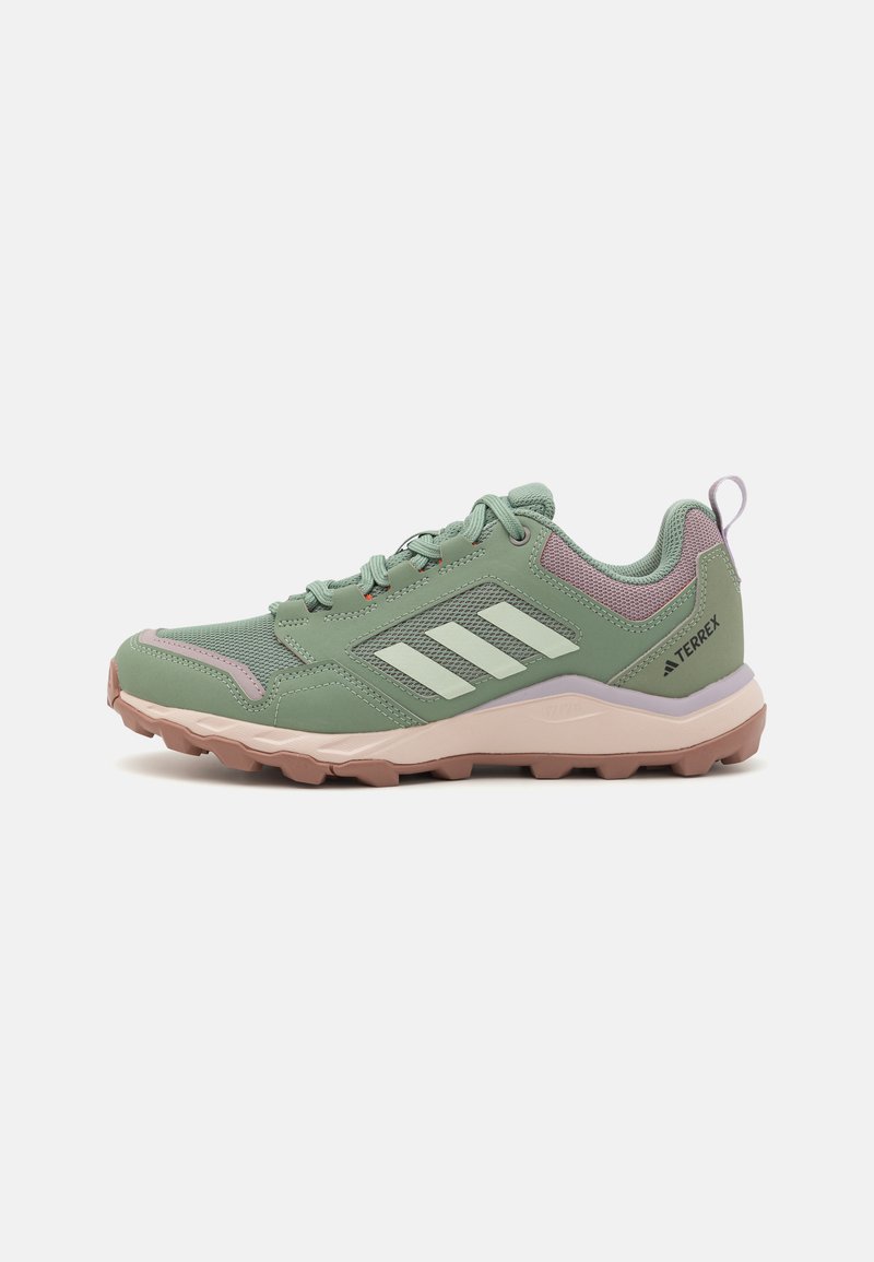 Groene sportieve schoenen met een gestructureerde mesh bovenkant, een beige rubberen zool en subtiele paarse accenten, met drie witte strepen aan de zijkant.