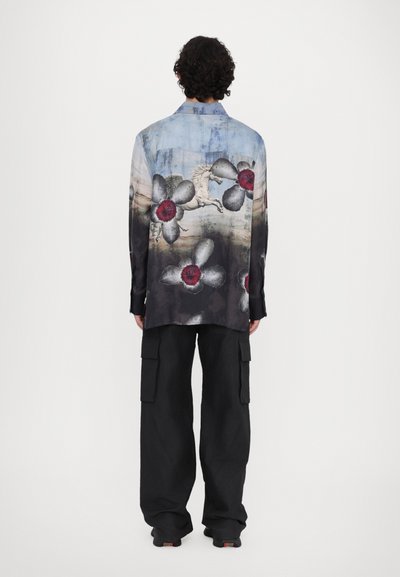 Shirt with blue and black abstract floral design, featuring a pegasus print; long sleeves and relaxed fit. Paired with loose black cargo pants.