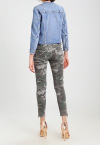 Světle modrá denimová bunda s dlouhými rukávy, v kombinaci se šedými maskáčovými slim-fit džíny a béžovými lodičkami na podpatku se šněrováním.