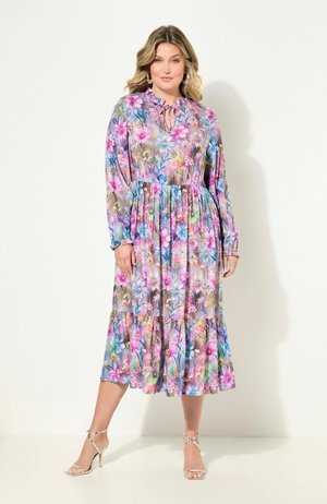Floral maxi dress in lightweight fabric with a ruffled hem. Features long sleeves, a tie neckline, and vibrant pink, purple, and green patterns.