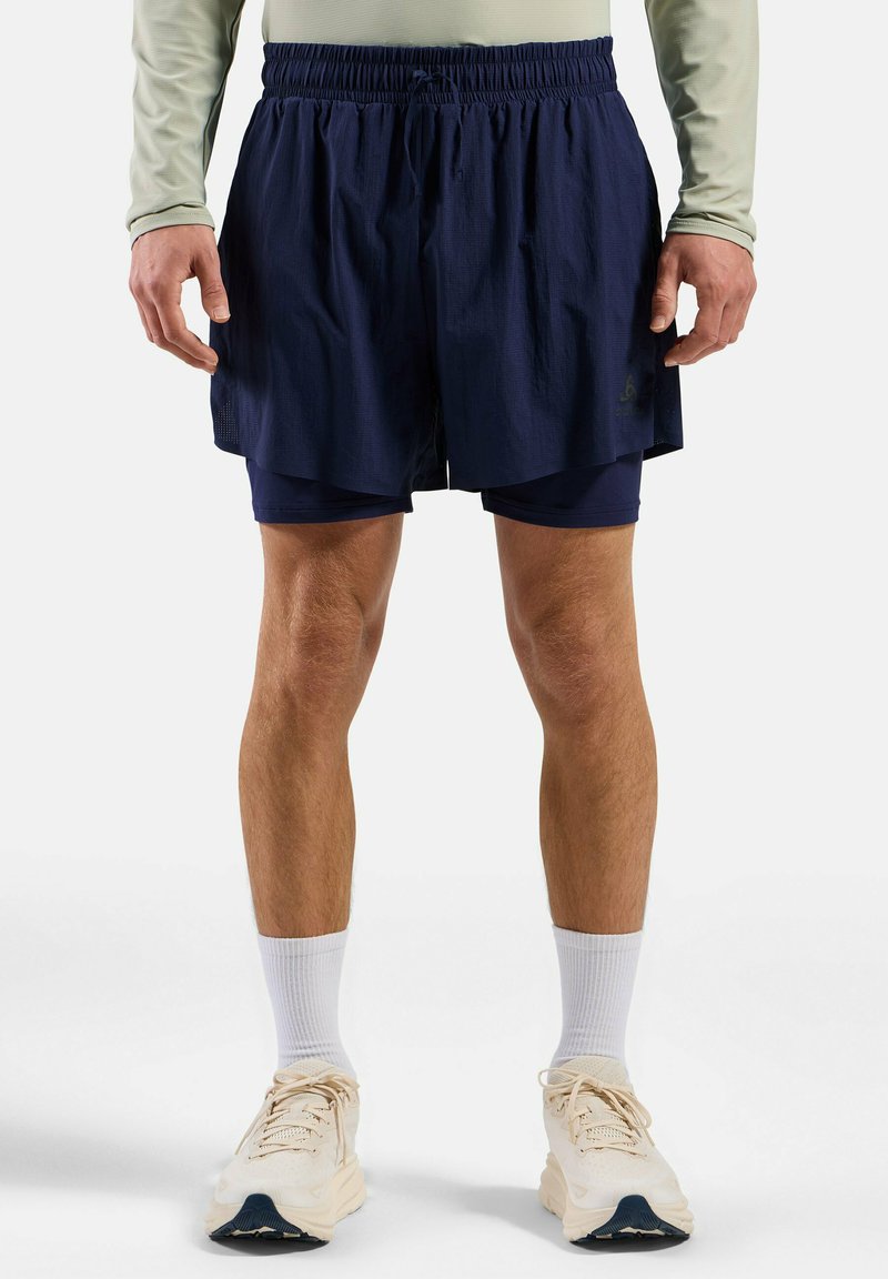 Shorts de course bleu marine avec une taille élastique et une doublure intérieure, associés à des baskets claires et des chaussettes blanches chevillées.