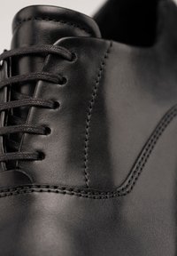 Gros plan sur une chaussure habillée en cuir noir montrant les lacets, les coutures et la texture lisse et polie.