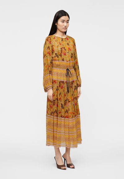 Μακρύ φόρεμα μουστάρδι με λουλουδάτα σχέδια, ελαστική μέση και κορδόνι. Μακριά μανίκια και στρωτό τελείωμα με αντιθετικές λωρίδες.