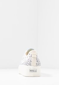 Vit kanvas sneakers med paisley-mönsterdetaljer, rund tå och en texturerad vit sula. Har en bakre dragflik och logotyp.