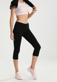 Jasnoróżowy sportowy stanik z perforowanym wzorem, czarne legginsy capri oraz jasnoróżowe buty sportowe. Gładkie, dopasowane materiały z wysokim stanem.