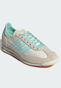 Baskets Adidas avec un design gris clair et turquoise, en matériaux en daim et synthétiques, trois bandes, et une semelle en caoutchouc texturée.