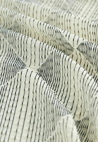 Tissu avec un motif texturé de lignes et formes noires sur un fond crème. Tissu doux, drapé avec une apparence ondulée.