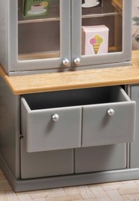 Armadio in plastica grigio con piano in legno, due porte in vetro e due cassetti con maniglie argentate. Contiene all'interno articoli alimentari colorati.