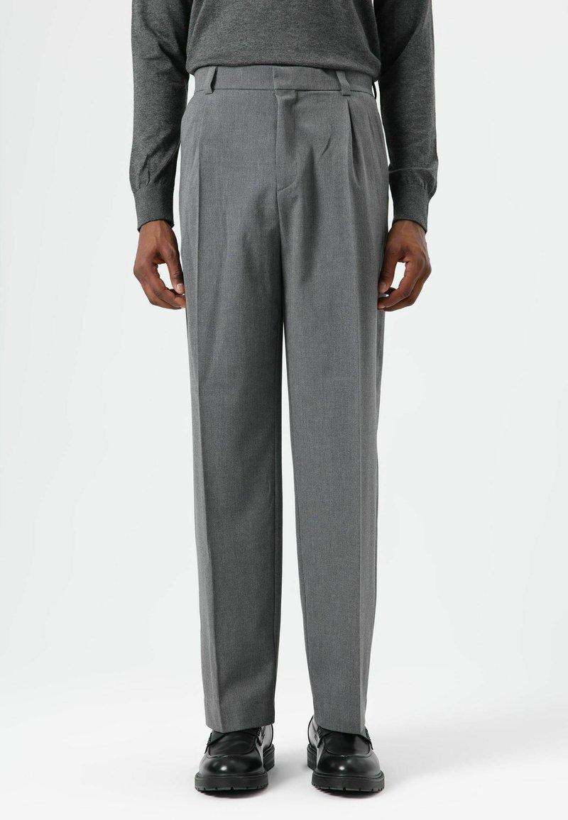 Pantalon gris sur mesure à jambe droite, avec des plis, une texture lisse et des passants pour ceinture, assorti à des chaussures noires à lacets.