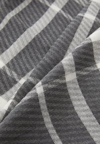 Gray and white plaid fabric with a herringbone texture, featuring thick and thin vertical and horizontal stripes. Soft, woven material.