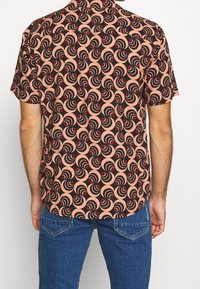 Chemise à manches courtes rose avec un motif tourbillonnant noir et rouge. Tissu léger, coupe décontractée, ourlet incurvé et col.