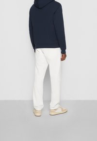 Námořnická mikina s klokaní kapsou, bílé denimové kalhoty a krémové tenisky. Jednoduchý design, uvolněný střih a kontrastní barvy.