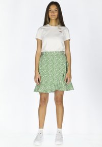 Gonna verde con stampa floreale e orlo svasato, abbinata a una t-shirt bianca a girocollo e sneakers bianche; tessuto morbido e vestibilità casual.