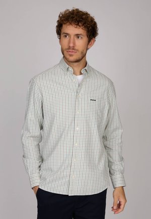 Chemise à manches longues, boutonnée, en tissu léger, arborant un motif à carreaux verts et rouges sur fond blanc, avec un logo sur la poitrine gauche.