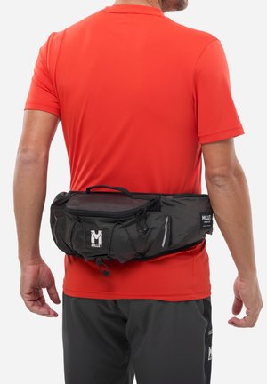 Homme portant une chemise rouge à manches courtes et une ceinture noire avec des poches zippées et le logo Millet sur le bas du dos.