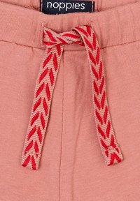 Ljusrosa bomullsbukser med en texturerad yta och ett vävt rött dragsnöre. Etikett "noppies" fäst vid midjan.