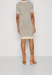 Robe en tricot à manches courtes en beige avec un motif de losanges noirs, col et poignets côtelés, silhouette ajustée et longueur mi-cuisse.