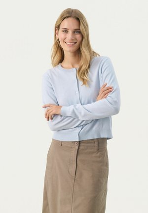 Cardigan léger bleu clair à manches longues avec un col rond et une fermeture à boutons, associé à une jupe beige au niveau des genoux avec un bouton à l'avant.