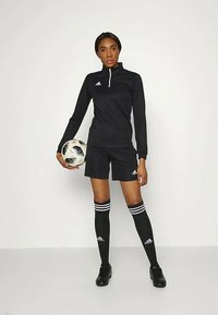 Czarny strój piłkarski z długim rękawem i szortami, z zamkiem w kołnierzu i białym logo Adidas; w zestawie z czarnymi skarpetami do kolan i korkami.