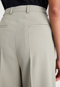 Beige op maat gemaakte broeken met een gladde textuur, voorzien van achterzakken en een aansluitende tailleband; ontworpen voor een gestructureerd silhouet.