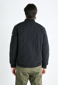 Gequilted zwarte bomberjack met een gestructureerde afwerking, geribbelde manchetten en zoom. Bevat een discreet logo op de linkermouw.