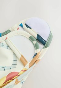 Värvikas kangas geomeetrilise mustriga, millel on erinevad kujundid. Sisaldab kahte ümarat valget kinnitusdetaili ja siledat tekstuuri.