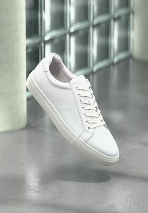 Baskets en cuir blanc avec lacets plats, bout rond et semelle texturée. Design épuré, mettant en avant un style minimaliste et des lignes nettes.