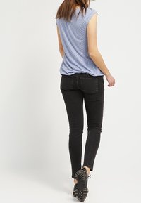 Ljusblå kortärmad topp med små vita prickar, matchad med svarta slim-fit jeans och svarta snörskor, sedd bakifrån.