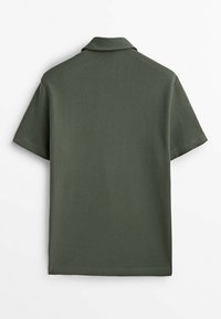 Polo à manches courtes de couleur vert foncé, fabriqué à partir d'un tissu texturé. Il présente un col ouvert et une coupe décontractée.