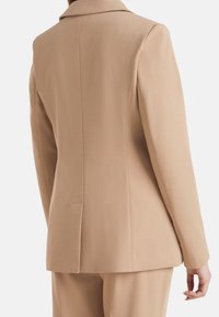 Beige sakový blazer s klopovým límcem, strukturovanými rameny, jedním rozventem na zadní straně a hladkou texturou tkaniny.