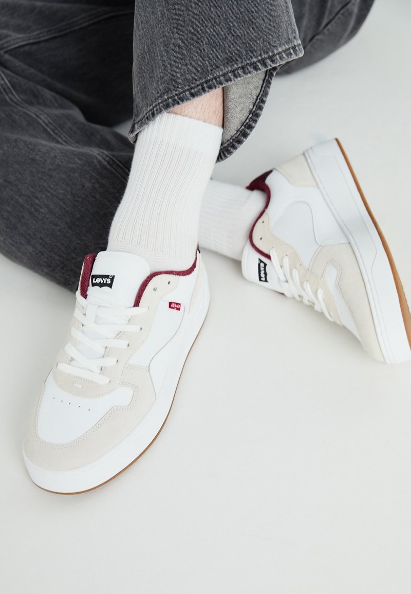 Bijele kožne tenisice s suknim akcentima u bež i maroon boji, s teksturiranom potplatom i crnim Levi's logotipom uz vezice.