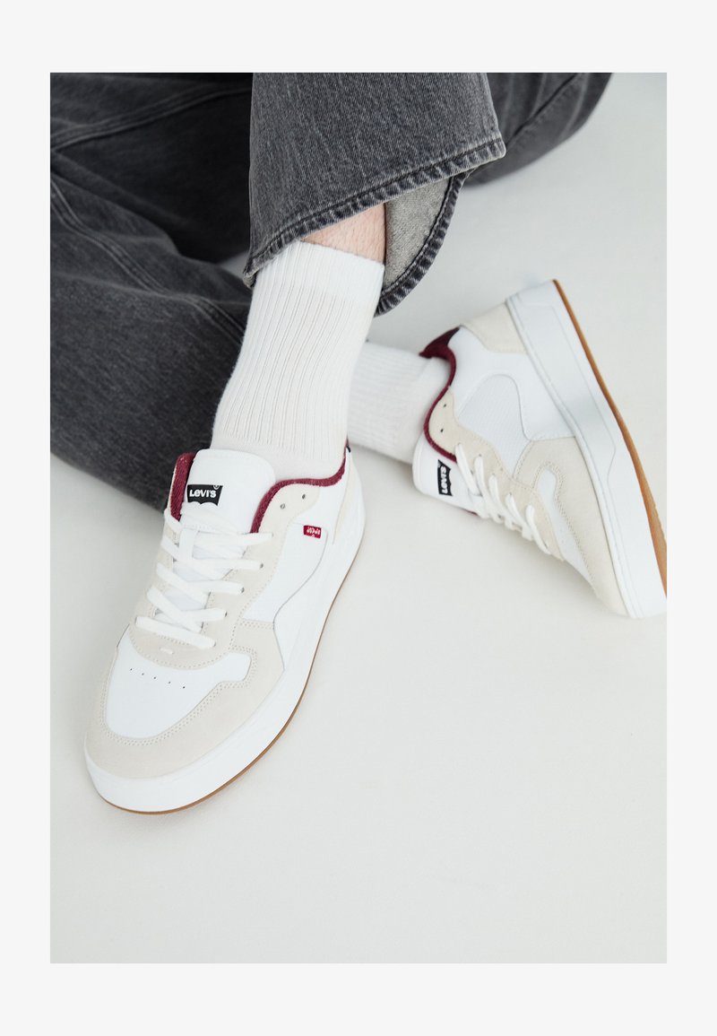 Bijele kožne tenisice s suknim akcentima u bež i maroon boji, s teksturiranom potplatom i crnim Levi's logotipom uz vezice.