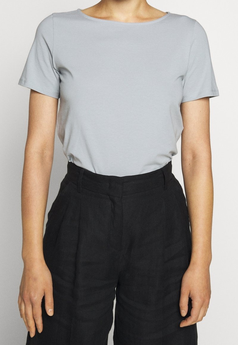 Lysegrå t-shirt med korte ærmer og rund hals, parret med højtaljede sorte linnedbukser med folder og struktureret stof.